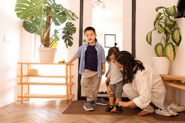A happy Asian family. A young attractive woman helps to take off her little daughter shoes.