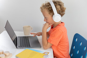 Little boy with white headphones and blonde hair, interacts with a laptop