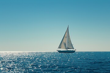 Fototapeta premium A lone sailboat with white sails glides across a calm, vast blue ocean under clear skies 