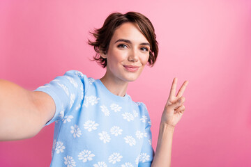 Portrait of pretty positive lady make selfie arm fingers demonstrate v-sign isolated on pink color...