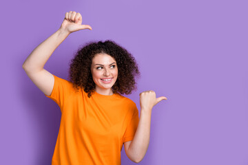 Photo of dreamy adorable woman wear orange t-shirt showing two thumbs looking empty space isolated purple color background
