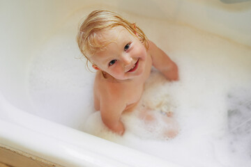 Portrait, bathtub and top view of happy baby girl in water for hygiene, health or wellness in bathroom. Foam, soap and face of kid bathing, clean skin and cute infant child with bubbles in home above