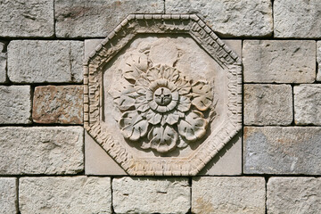 Fragment of a gray stone wall with an octahedral decorative flower motive rosette