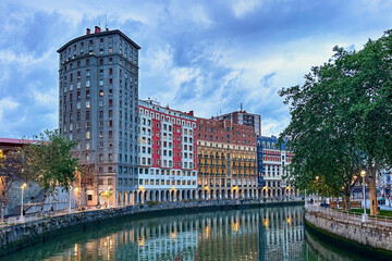 Colorful residential and apartment buildings and restaurants along the Nervion River in Bilbao, Spain on a cloudy sunset