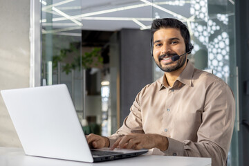Satisfied muslim male in headset with micro using contemporary gadget by white desktop at...