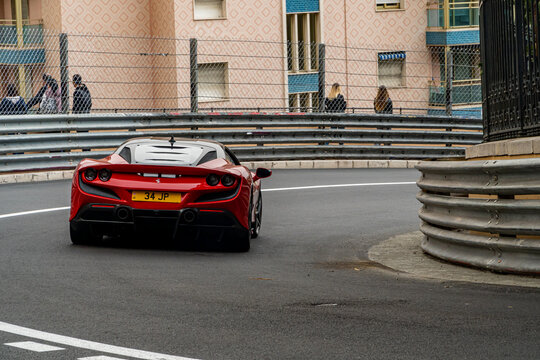Ferrari f8 spider red tribute version, turning right at the mirabeau haute curve of the Monaco formula 1 circuit, with the metal race fences in place.