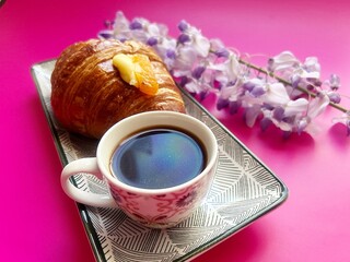 artisan croissant, fresh crispy croissant, puff pastry croissant, cornetto with cream, purple wisteria, pink background, cup with coffee, small espresso
