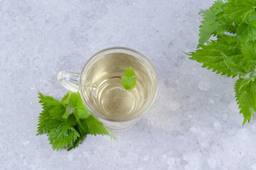 Herbal nettle tea and with fresh nettle leaves. Glass cup of nettle tea on a gray background....