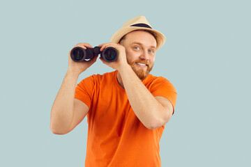 Curious Caucasian bearded man tourist smiles at the camera holding binoculars in hands, expressing...