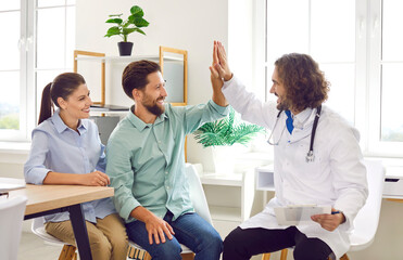 Happy family couple visit doctor together. Cheerful, smiling married man and woman give high five...