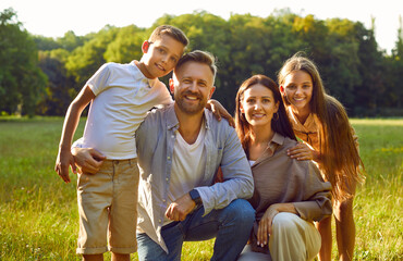 Portrait of happy smiling family with son and daughter sitting on green grass in the summer park...