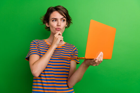 Photo portrait of lovely young lady netbook look skeptical touch chin dressed stylish striped garment isolated on green color background