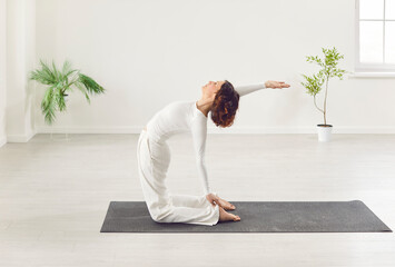 Sporty slim woman practicing yoga, stretching in Camel exercise, Ustrasana pose on mat, working out...