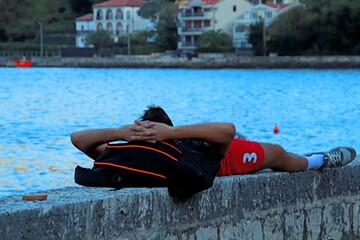 A young man in bright red shorts lies with his hands behind his head on the parapet of the Bay of...
