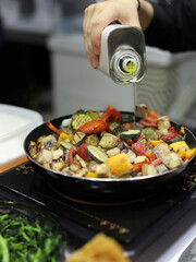 cocinero cocinado un plato de verduras y aliñándolas con aceite de oliva en el fogón de la cocina