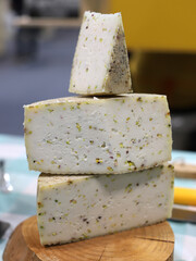 cuñas y mitades de quesos artesanales con ingrediente de pistacho en una tabla de madera en el...