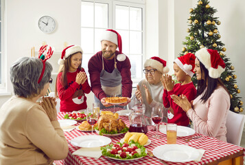 Family has Thanksgiving dinner sitting at table enjoys pie in dad's hands in festive living room at home. Grandparents, parents and children in Santa hats. Celebrating Christmas, New Year concept.