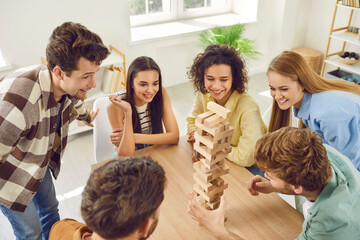 Top view photo of a happy young friends guys and girls playing together with wooden building blocks...