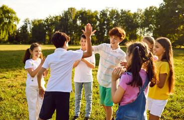 Group of a happy kids having fun and giving each other high five when they meet while walking in the summer park in nature. Cheerful children friends laughing outdoors. Friendship concept.