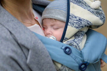 Close up of a baby sleeping in a baby carrier on his mother's chest or cleavage, in an...