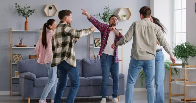 Group of happy, cheerful friends having fun at a party at home. Joyful energetic young people dancing together to lively music in a modern living room interior