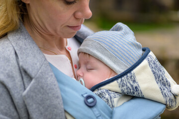 Close up of a baby sleeping in a baby carrier on his mother's chest or cleavage, in an...