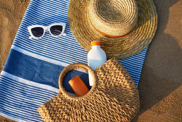 Sunbathing accessories on sandy beach, straw hat beside sunglasses, sunblock lotion in bag for skin...
