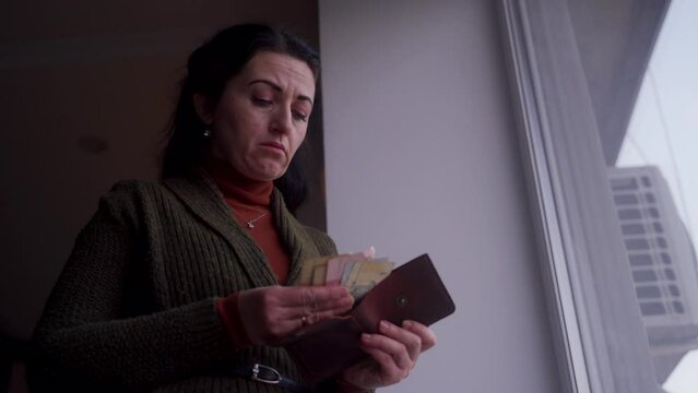 Concerned woman inspects empty wallet, anxiety evident as she finds no money. Urgent need, job hunt, financial crisis evident in her troubled expression indoors.
