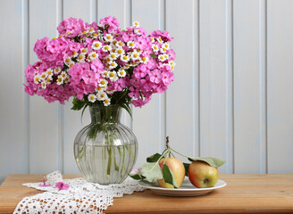 phlox and daisies on the table in a vase and apples.