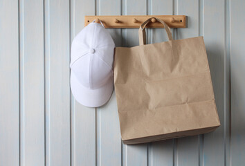 white baseball cap and a brown paper bag hang on a wooden hanger on a white board wall. Copy space. no plastic. natural interior.