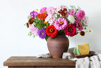 bright garden flowers, zinnias and asters, in a clay jug. still life with a bouquet and a piece of pumpkin.