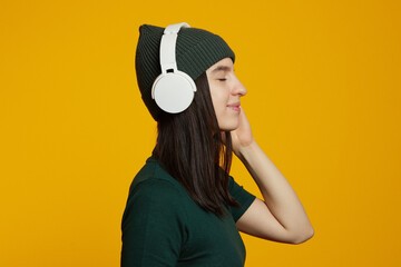 Side view of a cheerful young caucasian woman listening to music with wireless headphones isolated...
