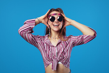 Joyful happy excited hippie young woman in trendy sunglasses, holding hands on head and smiles...