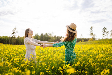 Two beautiful women in the middle of a yellow rapeseed field. Nature, vacation, relax and...