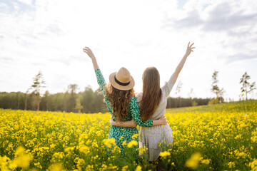 Two beautiful women in the middle of a yellow rapeseed field. Nature, vacation, relax and...