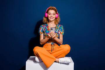 Full size photo of pretty young woman sit cube use phone wear top isolated on dark blue color background