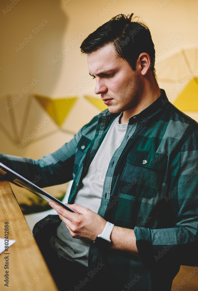 Poster pensive hipster guy reading report from planner and analyzing accountings for project upset with dat