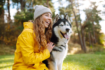 A young woman walks with her dog in the autumn forest. Husky dog.  Pet owner enjoys walking her dog...