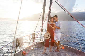 Traveling on yacht by sea at sunset. Happy couple in love drinking wine on sailboat. Travelers...