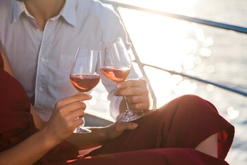 Drinking wine on yacht at sea. Two wineglasses in hands of couple in love at sunset. Man and woman...