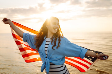 Cheerful happy woman outdoors on the beach holding USA flag having fun. USA celebrate 4th of July....