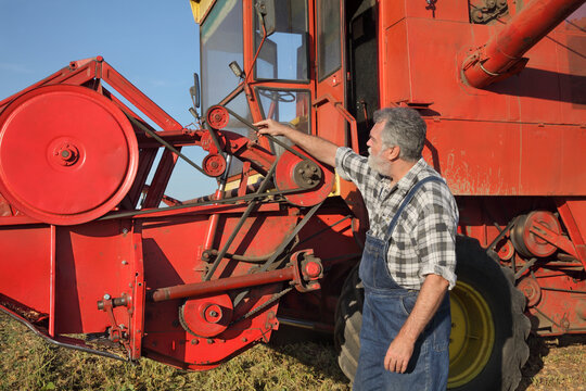 Adult farmer or mechanic touching and examining belt at combine harvester