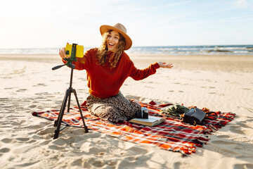 Style woman using smartphone with stabilizer, taking pictures and live video on the seashore. Travel, technology concept.