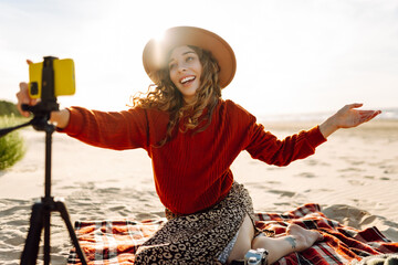 Style woman using smartphone with stabilizer, taking pictures and live video on the seashore. Travel, technology concept. - Powered by Adobe