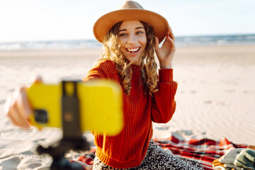 Style woman using smartphone with stabilizer, taking pictures and live video on the seashore. Travel, technology concept.