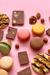 Pastel macarons, almond chocolate, peanut butter cookies and various nuts on bright pink background. Selective focus.