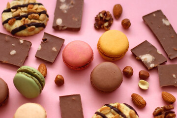 Pastel macarons, almond chocolate, peanut butter cookies and various nuts on bright pink background. Selective focus.