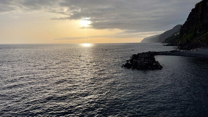 A serene sunset over the Atlantic Ocean, casting soft light on the water and rocky coastline of Madeira Island