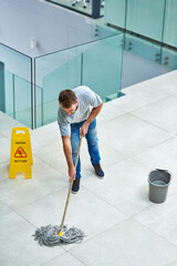 Man, janitor and mopping office floor or cleaning hygiene with caution sign or water, soap or...