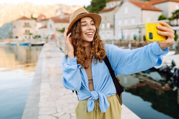 Young woman walks the streets and takes selfie using smartphone camera. Concept of positive...